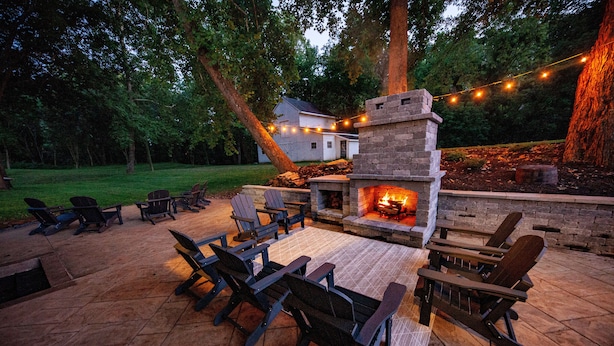 Une terrasse extérieure avec une cheminée en pierre, des chaises en bois et des guirlandes lumineuses.