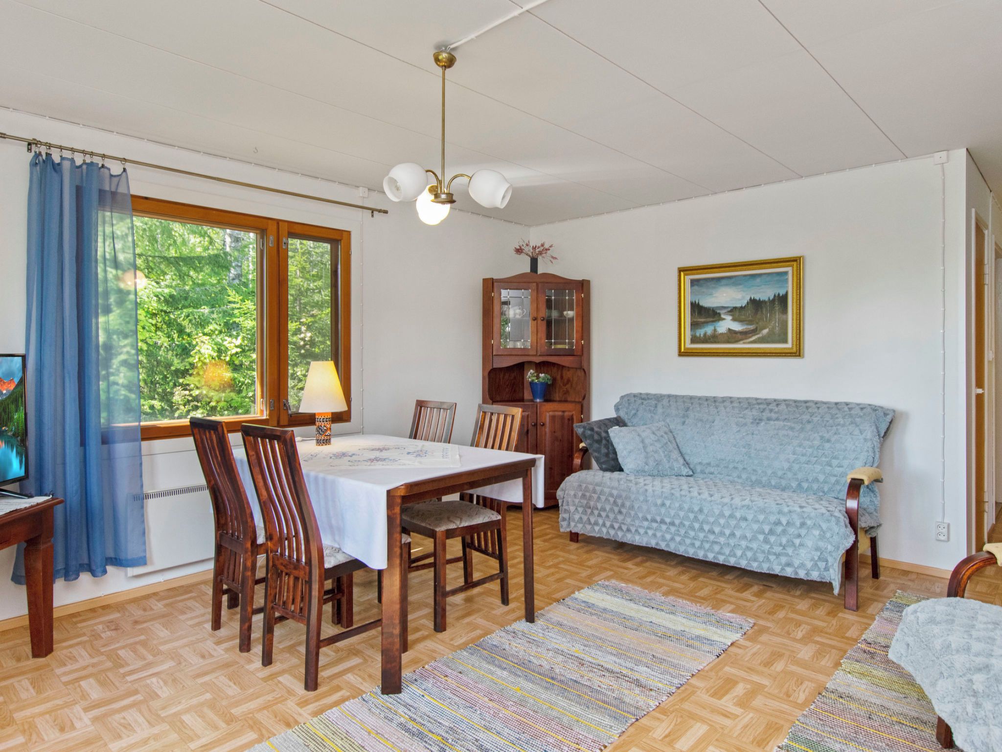 Ein Zimmer mit Esstisch, Stühlen, einer Couch, einem Schrank und einem Gemälde an der Wand.