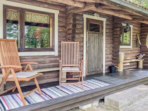 A log cabin with a porch, two wooden chairs, a door, and a window with a curtain. - Lamminranta by Interhome (Lemi)
