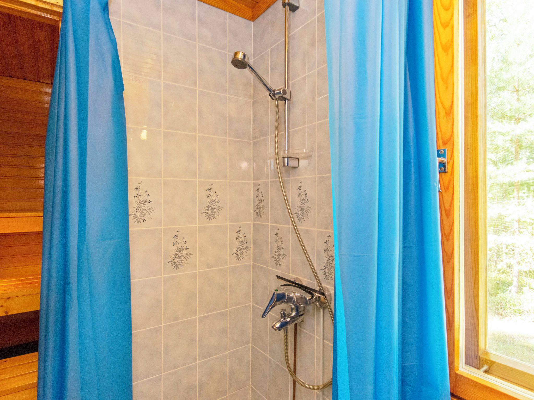 A shower with a handheld showerhead and a wall-mounted faucet, set against a tiled wall with floral patterns.