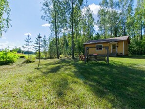 A wooden cabin with a porch and a bench, surrounded by a grassy yard and trees. - Lamminranta by Interhome (Lemi)