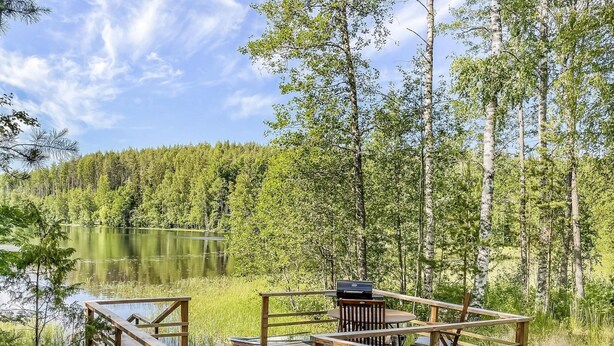 A wooden deck with outdoor seating and a grill, overlooking a lake and forest. - Lamminranta by Interhome (Lemi)