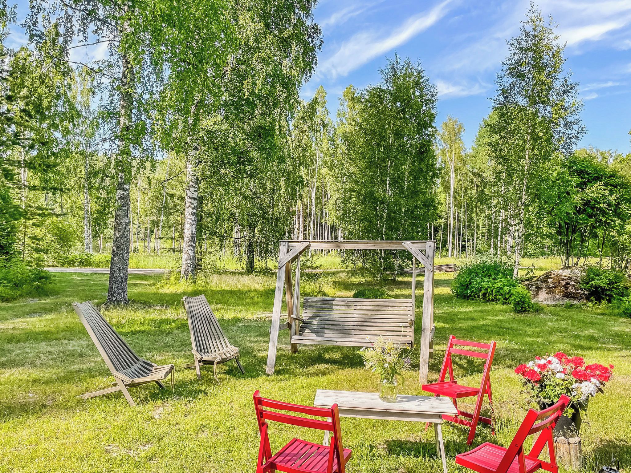 En träbänk och några stolar i ett grönområde, med en träpergola och ett bord.