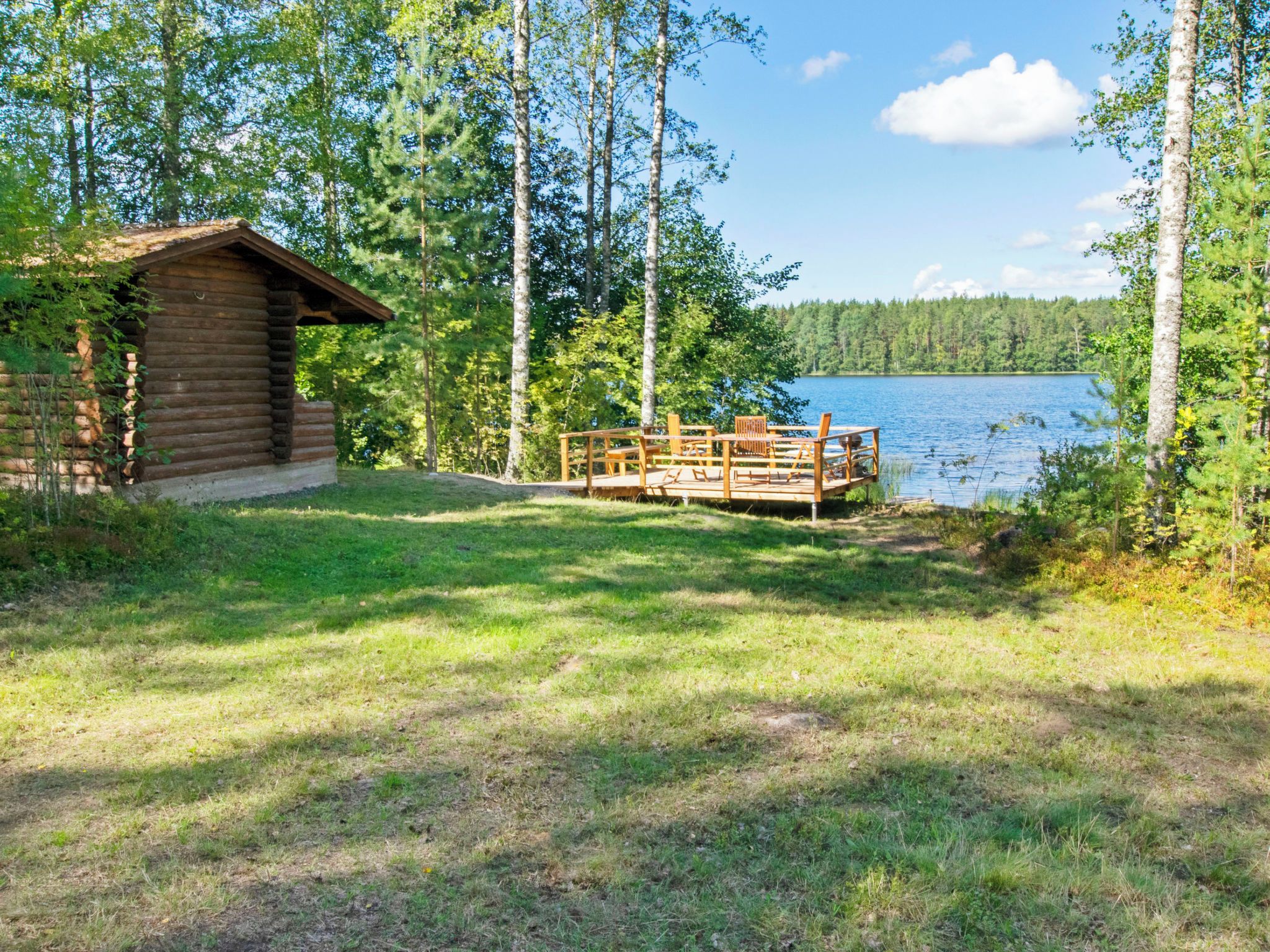 A log cabin with a deck overlooking a lake, surrounded by trees.
