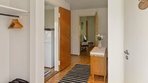 A hallway with a wooden door, a white wall, a wooden floor, a small table with a vase, and a hanging rack with clothes. - Lamminranta by Interhome (Lemi)