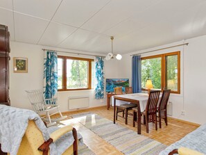 A room with a dining table, chairs, a rocking chair, a radiator, and large windows with curtains. - Lamminranta by Interhome (Lemi)