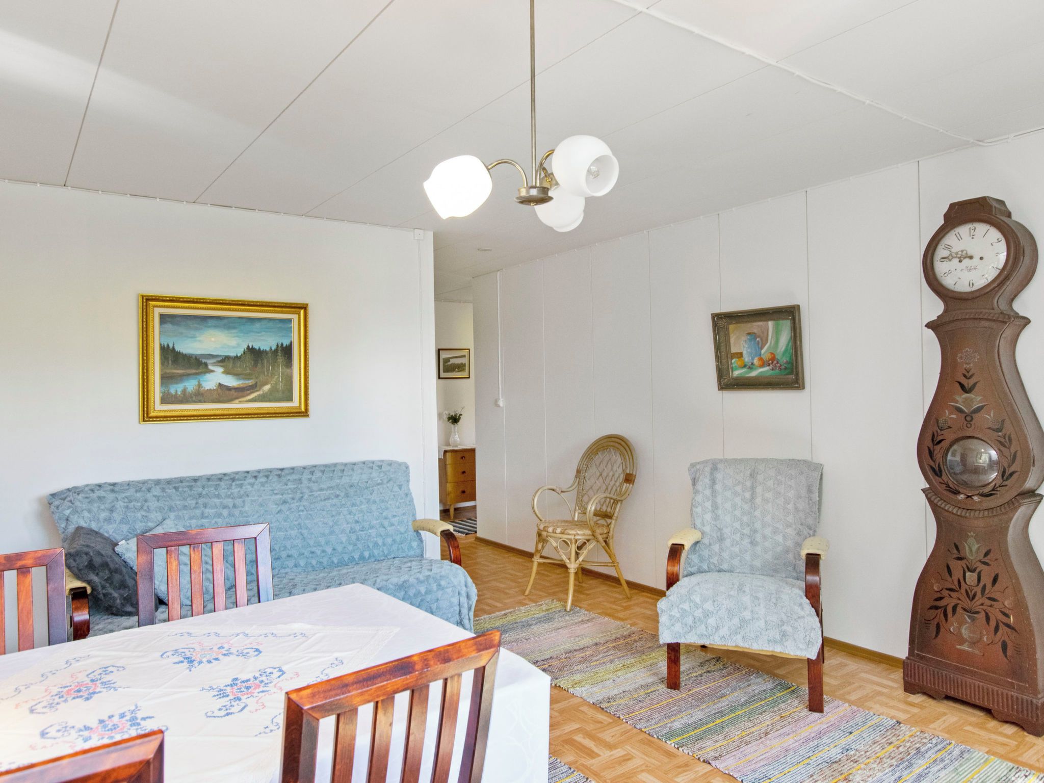 A living room with a sofa, chairs, a dining table, a clock, and artwork on the walls.