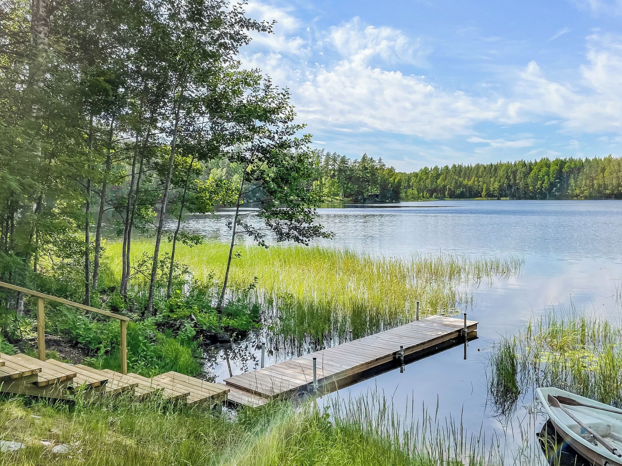 A calm lake with a wooden dock extending into the water, surrounded by lush greenery and trees.