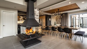 A modern living room with a large fireplace, a dining area with a wooden table and chairs, and a kitchen in the background. - NEW! La Marie-Pierre Ski/Golf Mont Tremblant (Mont-Tremblant)