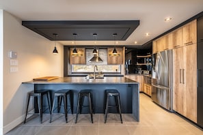 A modern kitchen with a central island, bar stools, pendant lighting, and stainless steel appliances.