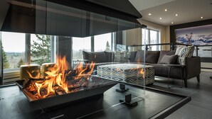A modern living room with a glass fireplace, comfortable seating, and a large window offering a scenic view. - NEW! La Marie-Pierre Ski/Golf Mont Tremblant (Mont-Tremblant)