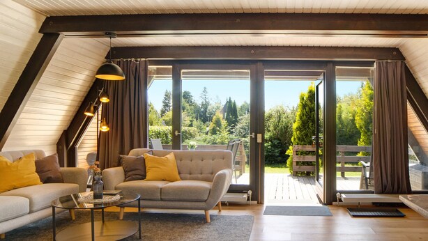 A loft-style room with a large sliding glass door leading to an outdoor deck, a sofa, a coffee table, and a pendant light. - Holiday Home 'Auszeit' with terrace & garden (Tennenbronn)