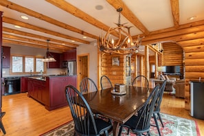 L’intérieur d’une cabane en rondins, avec une table à manger en bois, des chaises, un lustre et un coin cuisine.