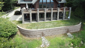 A log cabin with a stone foundation, large windows, and a covered porch.