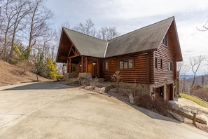 Une cabane en rondins avec un toit à forte pente, des fondations en pierre et une véranda à l’avant.
