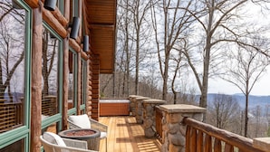 A wooden deck with stone railings, wicker chairs, and a hot tub.