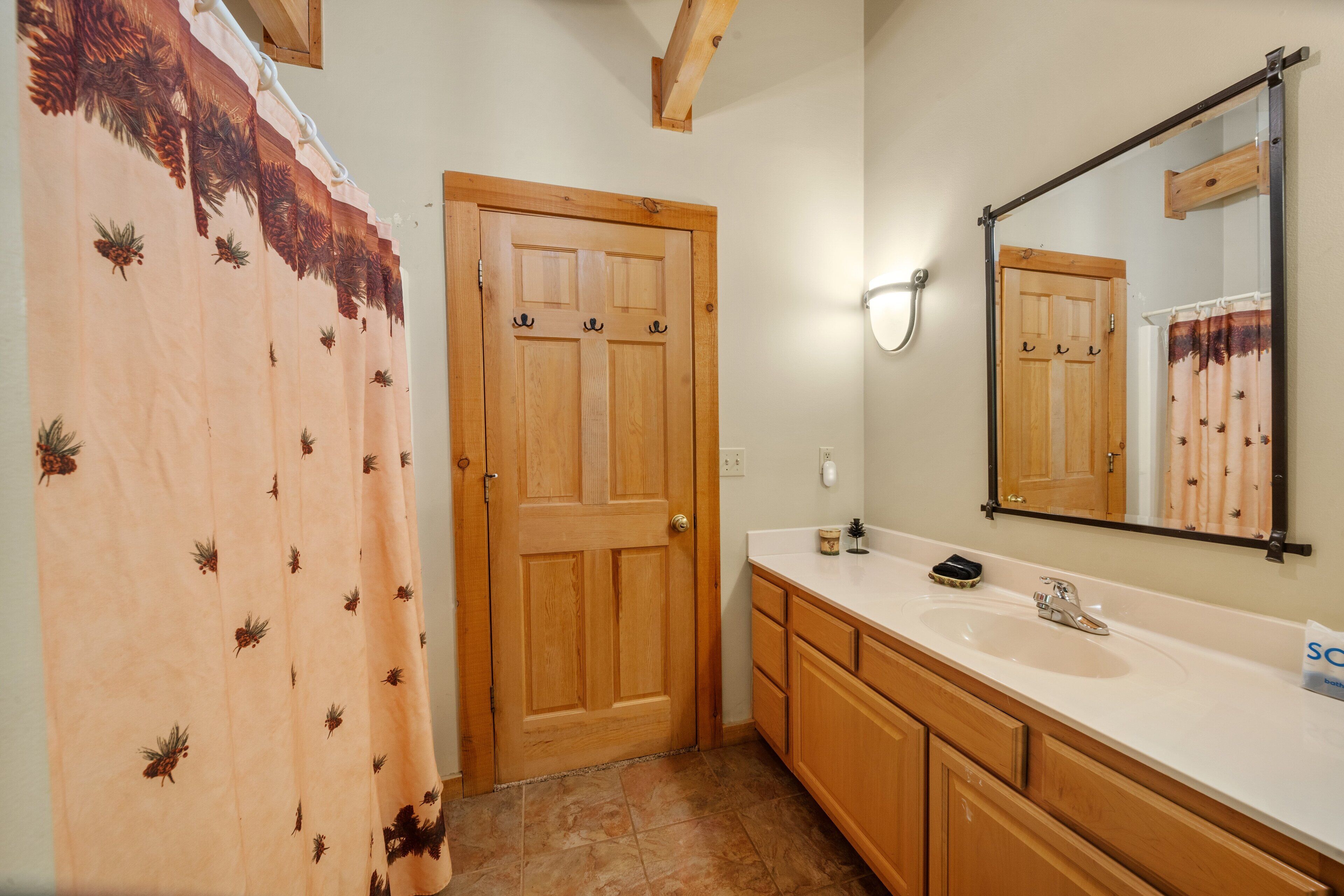 Un bagno con una porta in legno, un lavandino bianco, uno specchio e una tenda da doccia con motivi a pigna.