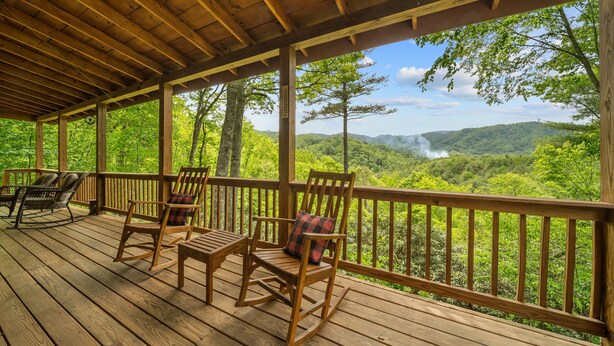 Une terrasse en bois avec des fauteuils à bascule et une table, offrant une vue sur un paysage boisé.