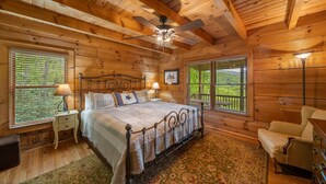 Une chambre dans une cabane en bois, comprenant un lit, deux tables de chevet, une chaise, une commode et un ventilateur de plafond.