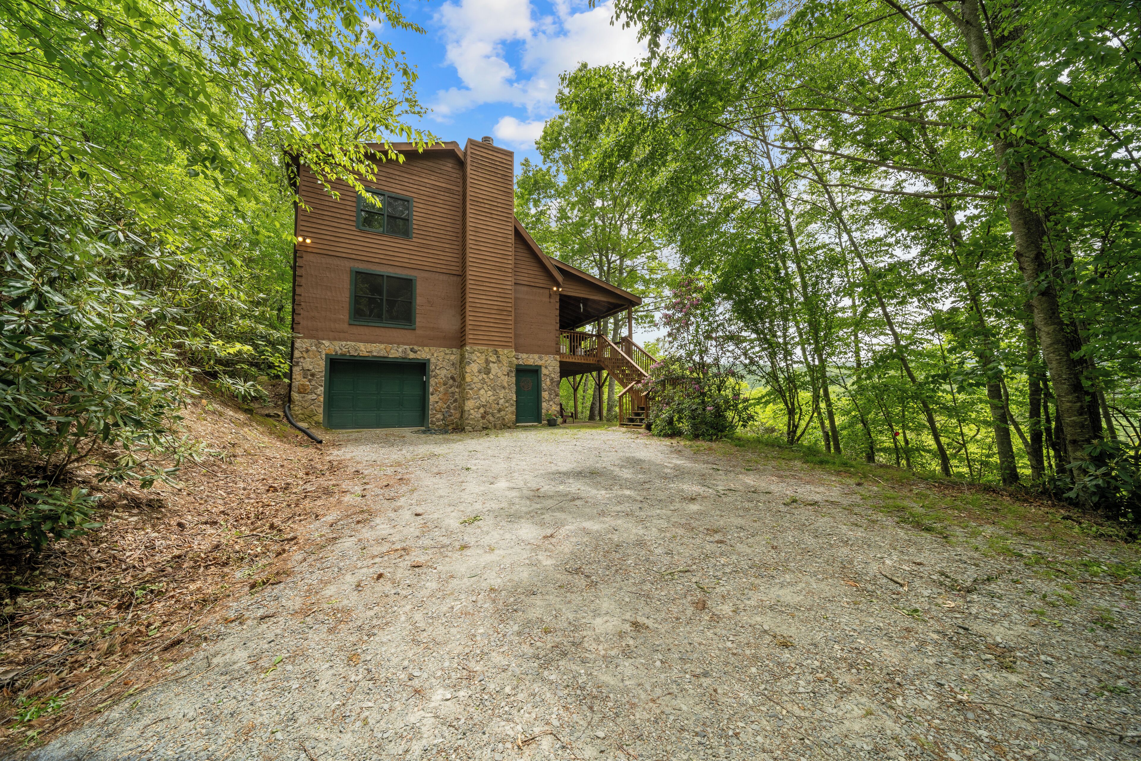 A rustic cabin with a stone foundation, a wooden exterior, and a green garage door.