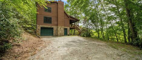 A rustic cabin with a stone foundation, a wooden exterior, and a green garage door.