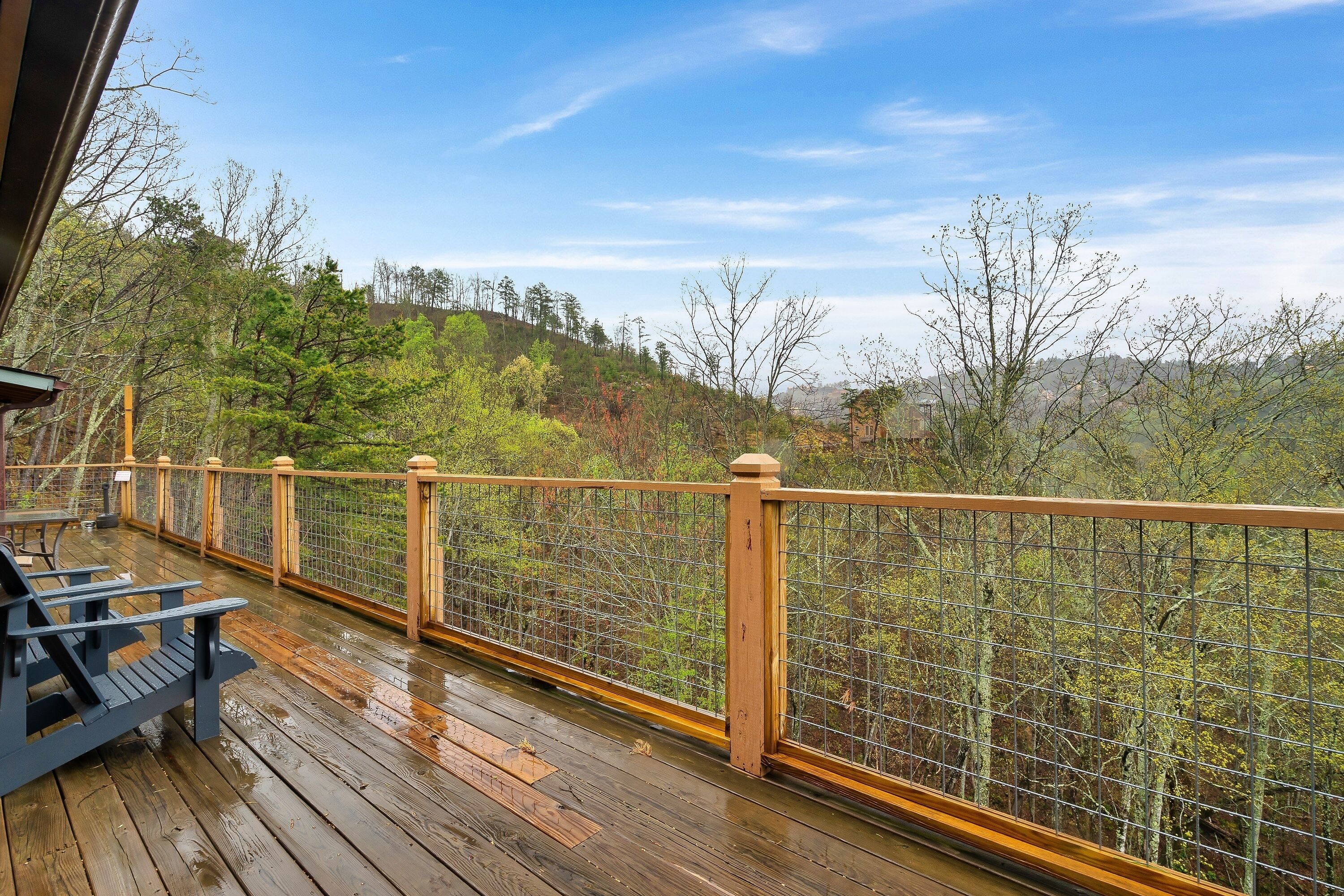 A wooden deck with a railing, overlooking a forested hillside.