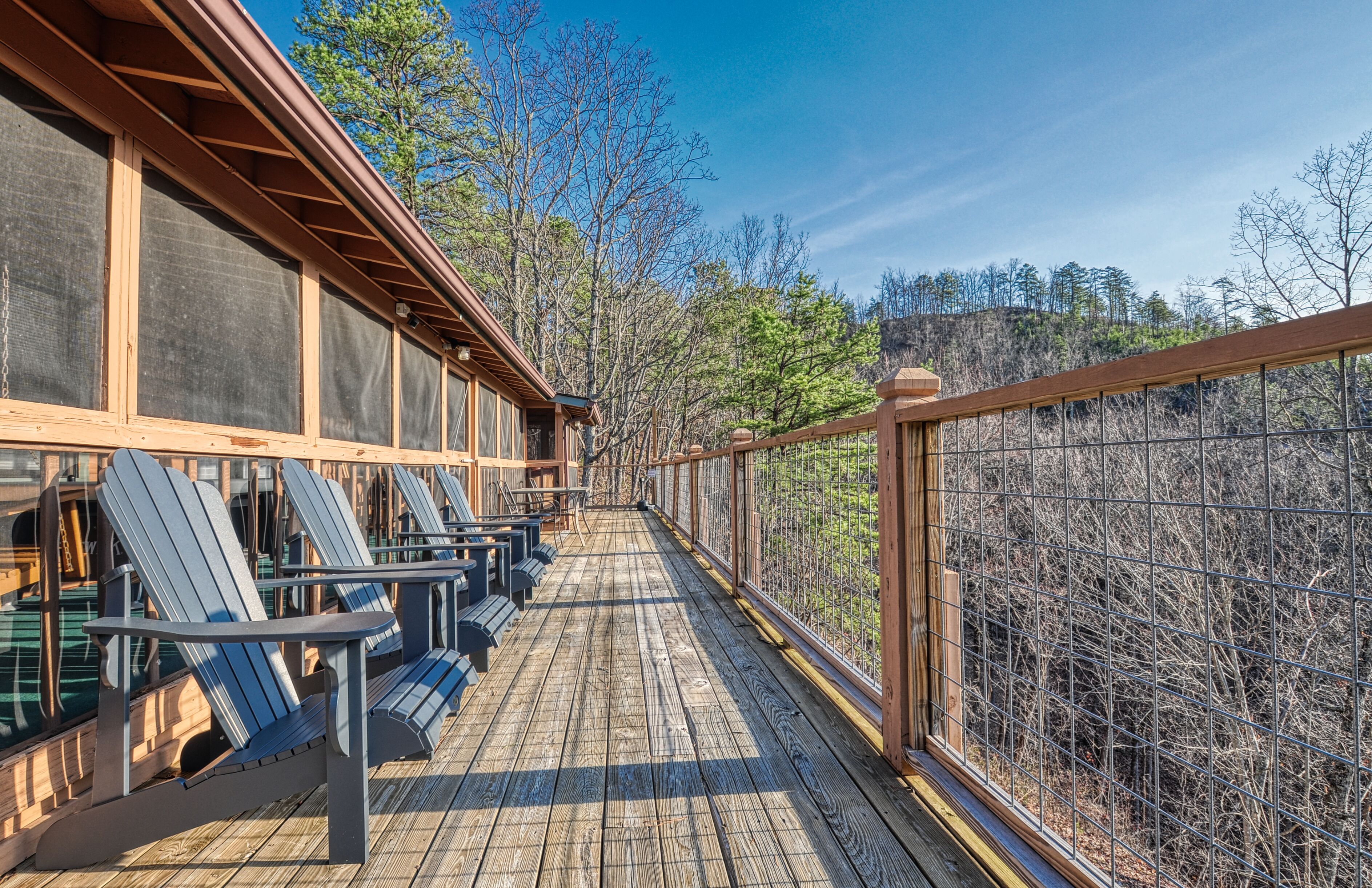 A wooden deck with Adirondack chairs and a view of a forest.