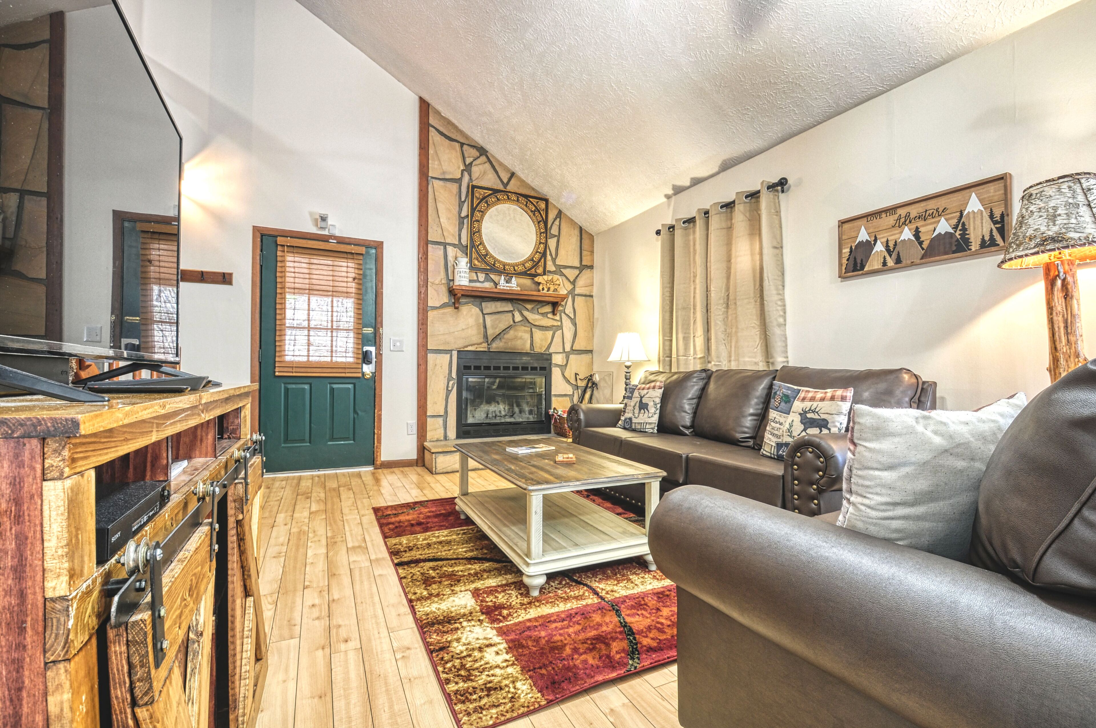 A cozy living room with a fireplace, a wooden coffee table, a leather sofa, and a stone wall with a mirror.