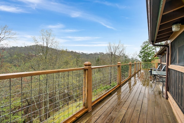 Une terrasse en bois avec une rambarde en métal, donnant sur une zone boisée.