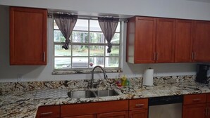 Une cuisine dotée de plans de travail en granit, de meubles en bois, d’un évier en acier inoxydable et d’une fenêtre agrémentée de rideaux.