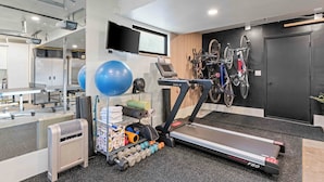 A modern gym with a treadmill, exercise balls, dumbbells, and bicycles.