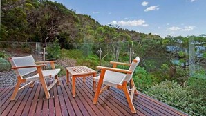 Une terrasse en bois avec deux chaises et une petite table, offrant une vue sur un paysage verdoyant et luxuriant ainsi que sur une étendue d’eau.