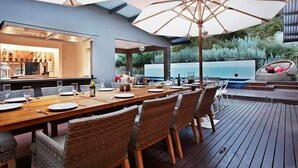 Un espace extérieur aménagé pour les repas, avec une terrasse en bois, des chaises en osier et un grand parasol.
