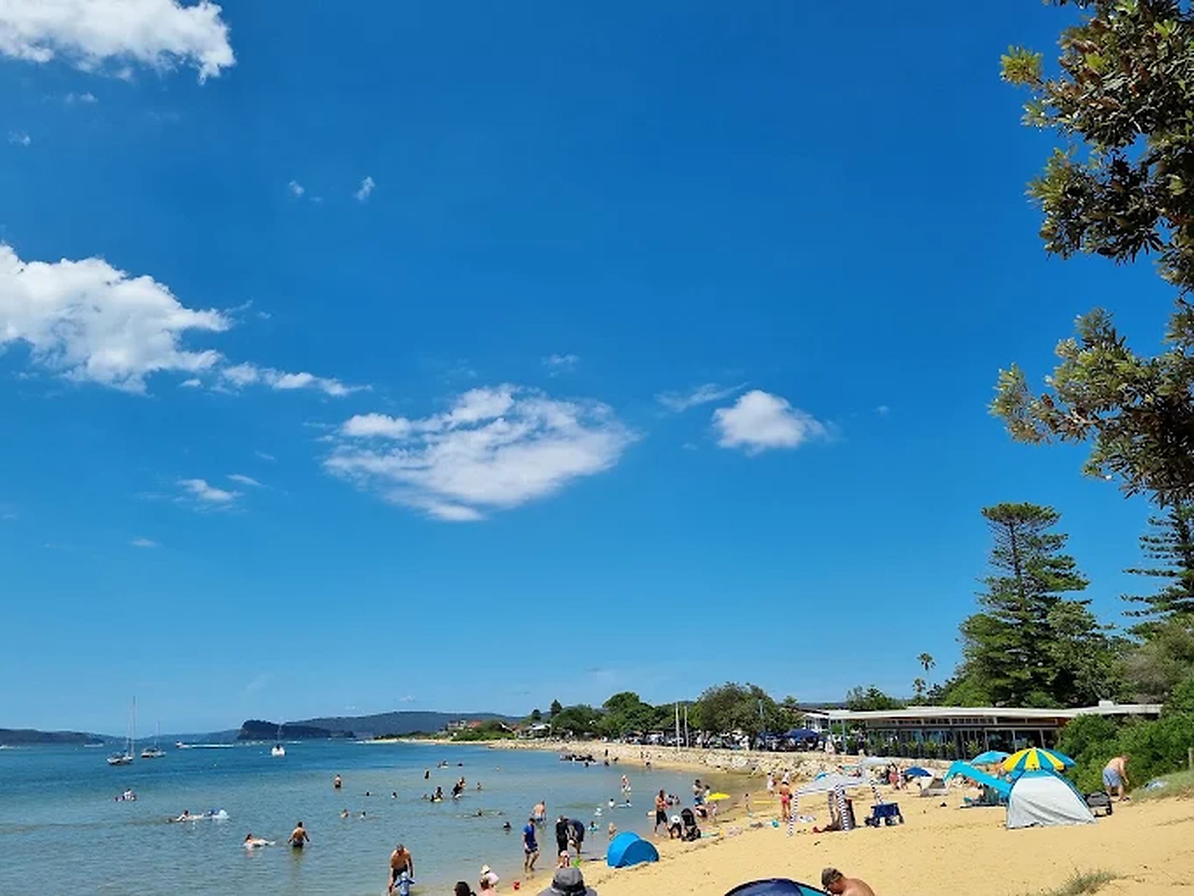 A beach with people swimming and sunbathing, tents, and boats in the water.