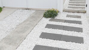 Ein moderner Außenweg führt zu einem Gebäude mit weißer Fassade und einer Satellitenschüssel auf dem Dach.