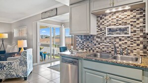 A modern kitchen with a tiled backsplash, a sink, and a dining area with a blue chair and table. - Great Location!! Family Friendly, 3 Pools, Lake, Tennis, Free Activities & Walk to Restaurants/Shops (Destin)