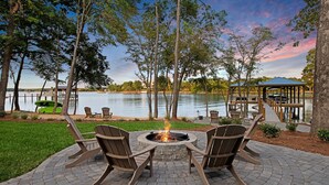 An outdoor seating area with a fire pit, surrounded by trees and a lake view. - Hanesbee Escape w/Beach, Hot Tub & Optional Boat Rental (Mooresville)