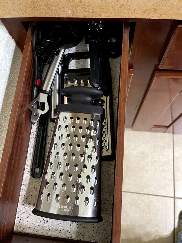 Un cajón de cocina con un rallador, un cuchillo y un abrelatas.