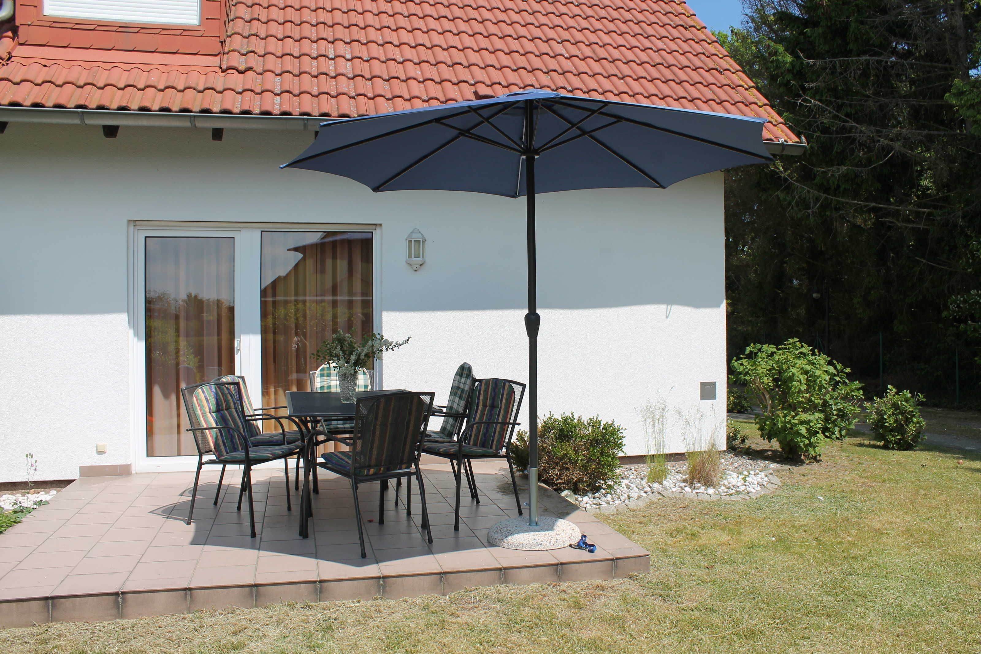 Um pátio com mesa e cadeiras, um guarda-sol e uma casa com telhado vermelho.