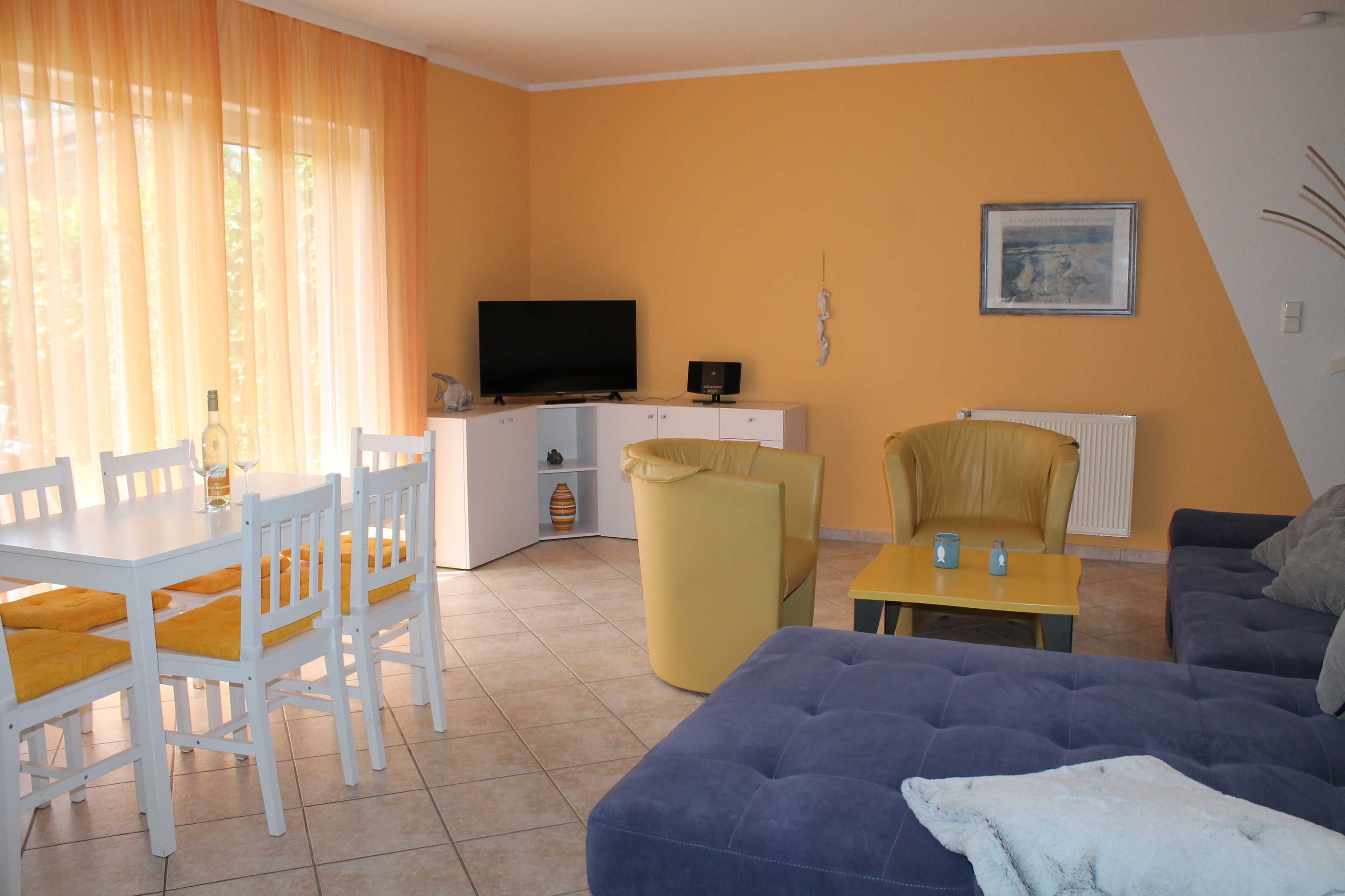 Een woonkamer met een televisie, bank, eettafel, stoelen en een radiator.