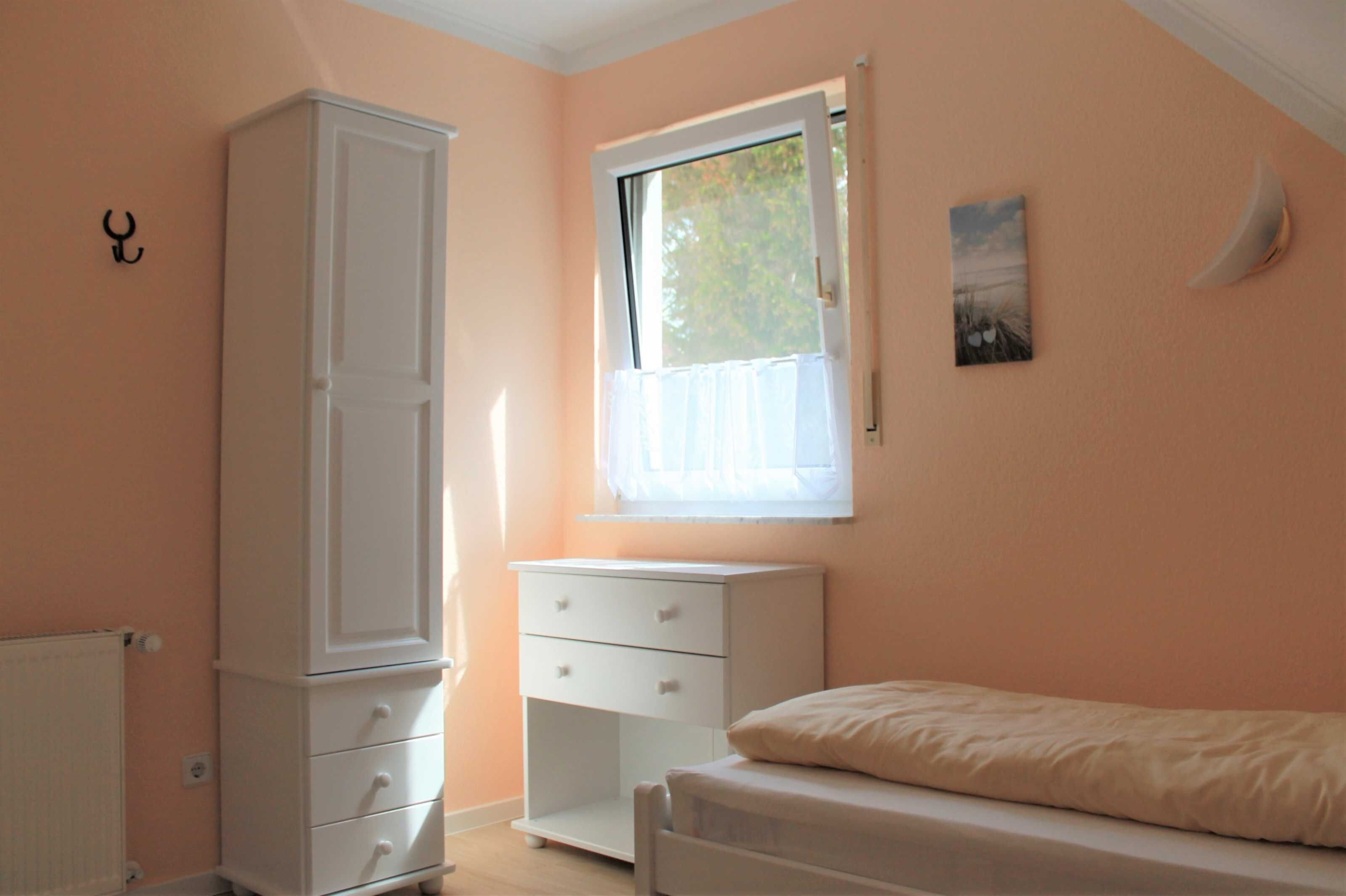 Un dormitorio con cama, ventana, armario y mesita de noche.