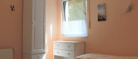 Un dormitorio con cama, ventana, armario y mesita de noche.