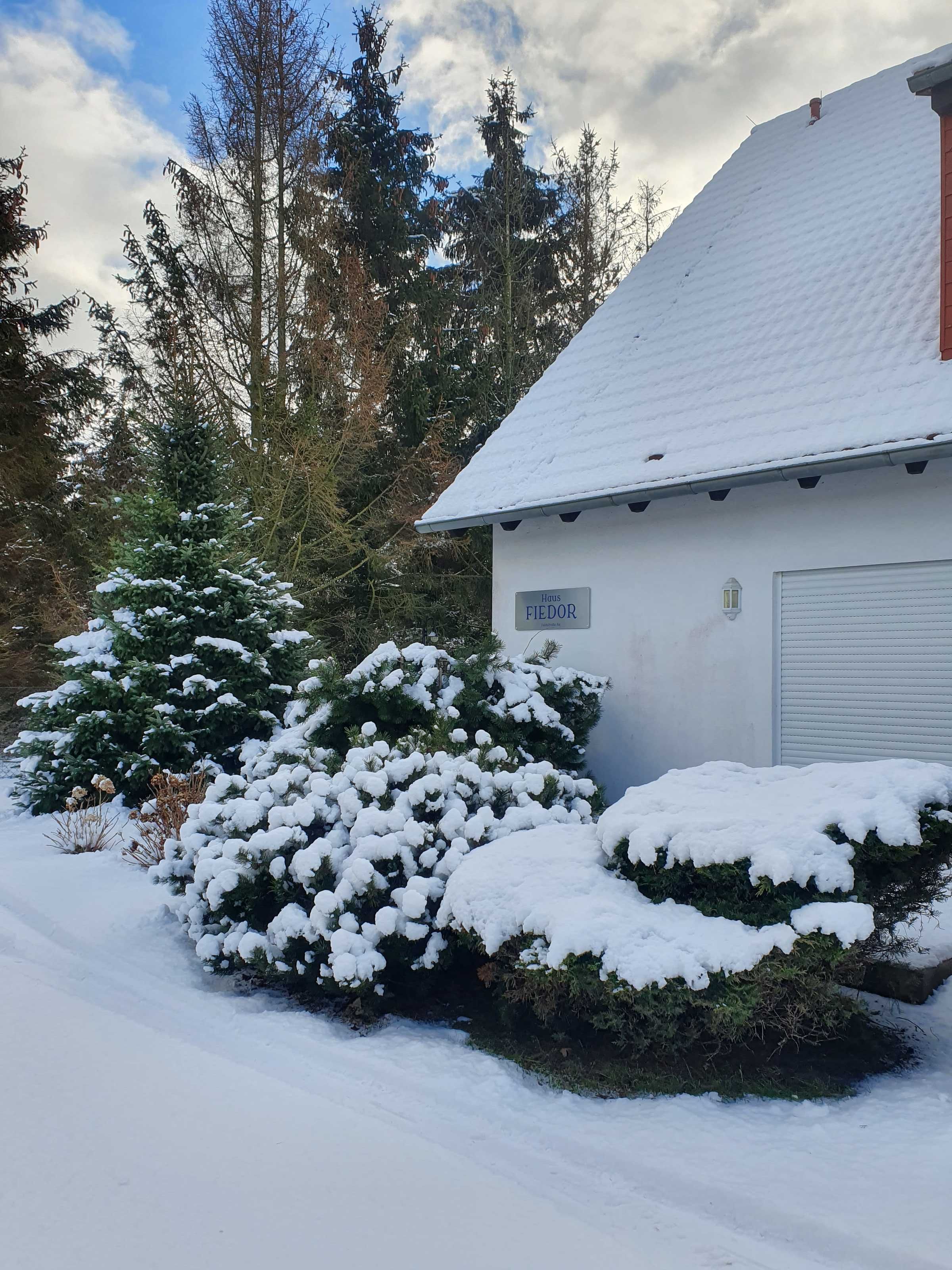 A snow-covered building with a sign reading 'Haus FIEDOR' and a garage door.