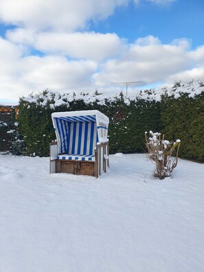 A snow-covered outdoor seating area with a striped chair and a small table, surrounded by snow-laden bushes and a hedge. - 3 R-Fewo Smutje - Haus Fiedor in the seaside resort of Zempin (Zempin)