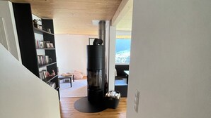 A staircase leading to a living area with a wood-burning stove, a bookshelf, and a view of the outdoors. - Modern, idyllic vacation home with breathtaking panoramic views (Gaschurn)