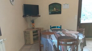 Un'area pranzo con un tavolo apparecchiato per quattro persone, una televisione a parete e una sveglia appesa al muro.