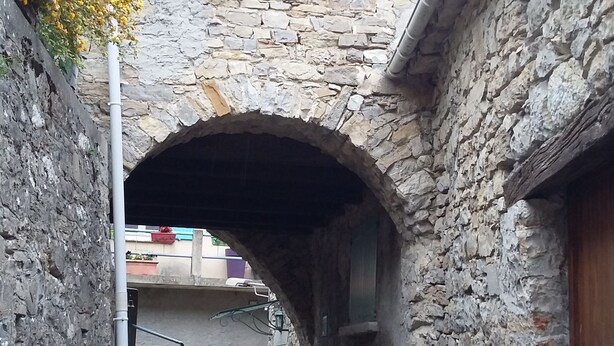 Un arco in pietra che conduce a un cortile con un muro in pietra su un lato e l'ingresso di un edificio sull'altro.