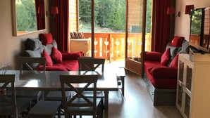 A modern living room with a dining area, large windows, and a view of a forested area. - Residence on the slopes with heated outdoor pool (Vars)
