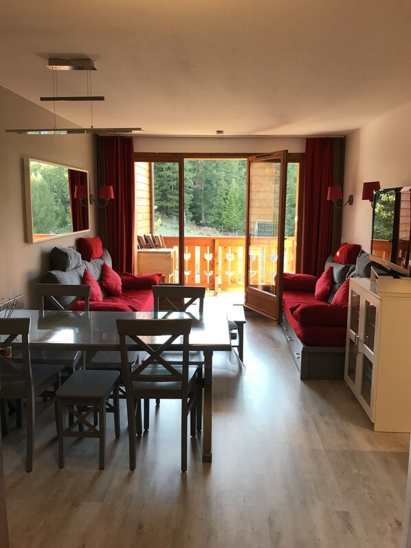 A modern living room with a dining area, large windows, and a view of a forested area.