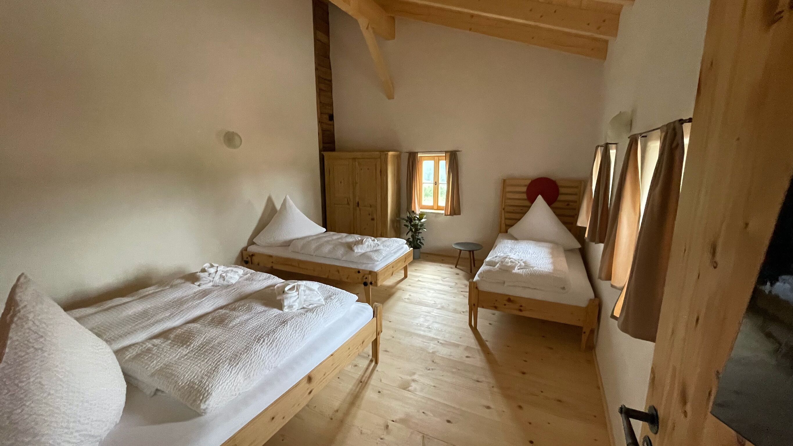 A room with two wooden beds, a small table, and a window with curtains.